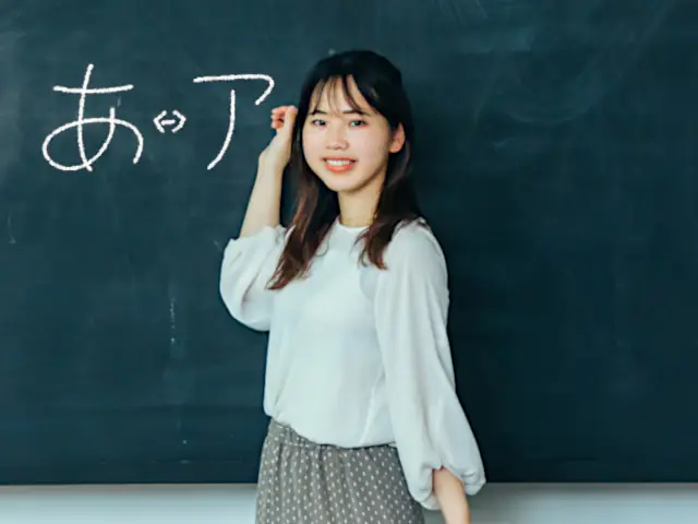 Japanese language teacher in front of a blackboard. Hiragana and Katakana are written on the blackboard. Find the perfect japanese language school in Tokyo with ENJ.
